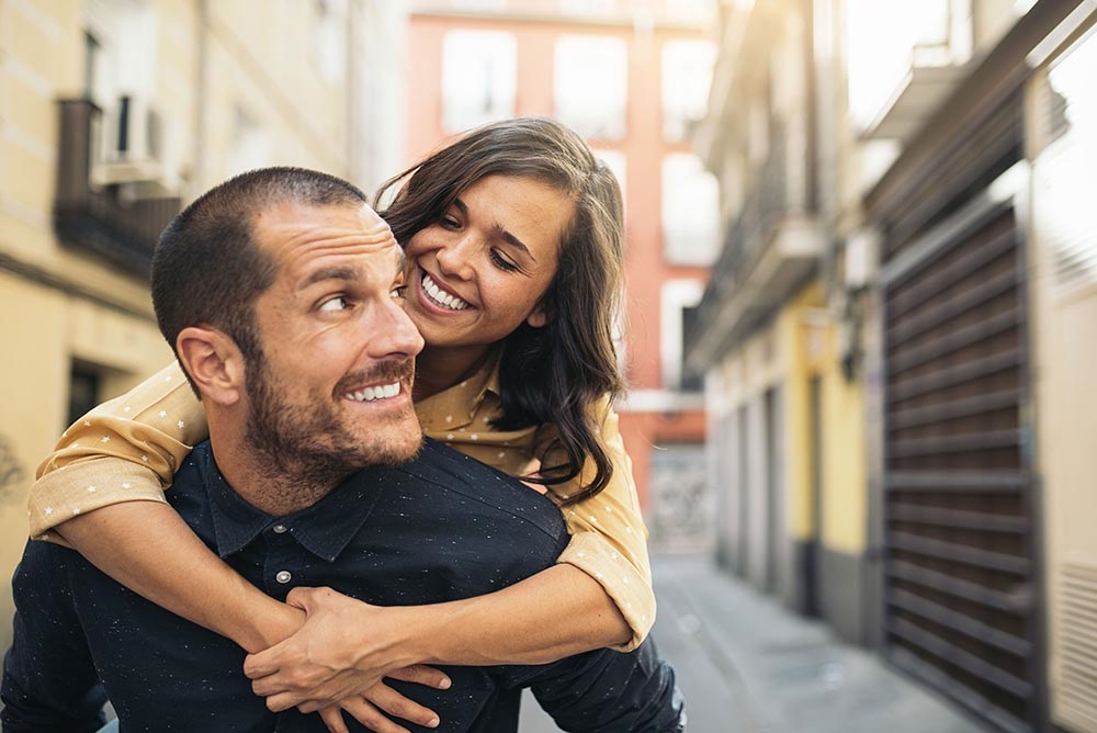 Couple enjoying a playful moment in a European street, embodying joy and connection, relevant to discussions on lifestyle impacts on oral health during adulthood.