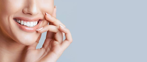 Smiling woman showcasing healthy teeth and hand gently touching her face, representing confidence and comfort during dental visits.